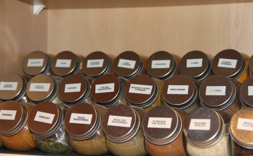 Labelled spice jars in alphabetical order on three-tiered shelf in cupboard. Julia Stewart photo.